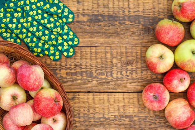 Rode appels in rieten mand en op oude houten planken met tuinhandschoenen. Bovenaanzicht met kopieerruimte