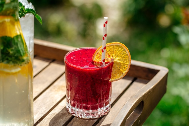 Rode bessen smoothie in een glas met een rietje op een houten dienblad