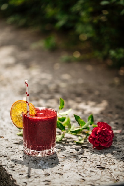 Rode bessen smoothie in een glas met een rietje op een steen met bloem