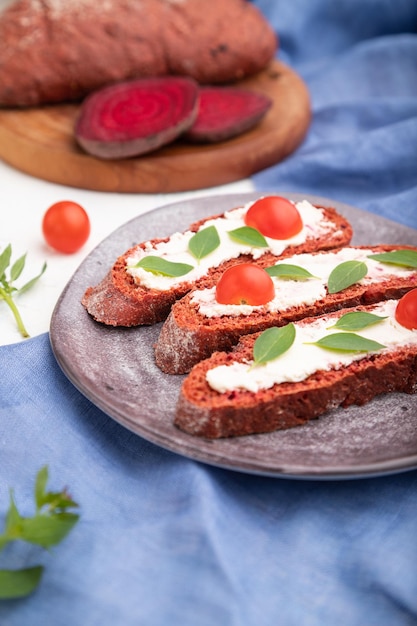 Rode bietenbrood sandwiches met roomkaas en tomaten op witte betonnen ondergrond en blauw linnen textiel. Zijaanzicht, selectieve focus, close-up.