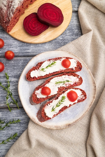Rode bietenbroodsandwiches met roomkaas en tomaten op grijze houten bovenaanzicht als achtergrond