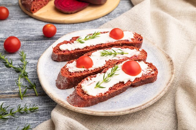 Rode bietenbroodsandwiches met roomkaas en tomaten op grijze houten oppervlakte en linnentextiel