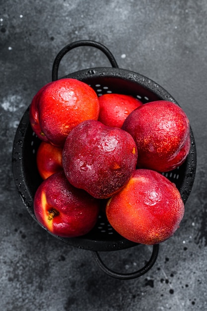 Rode biologische nectarines in een vergiet. Zwarte achtergrond. Bovenaanzicht.