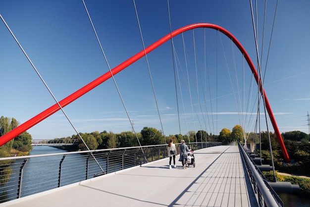 Foto rode brug over de rivier bij nordstern park met daarop vrouwen met een kinderwagen, schurenbachhalde.