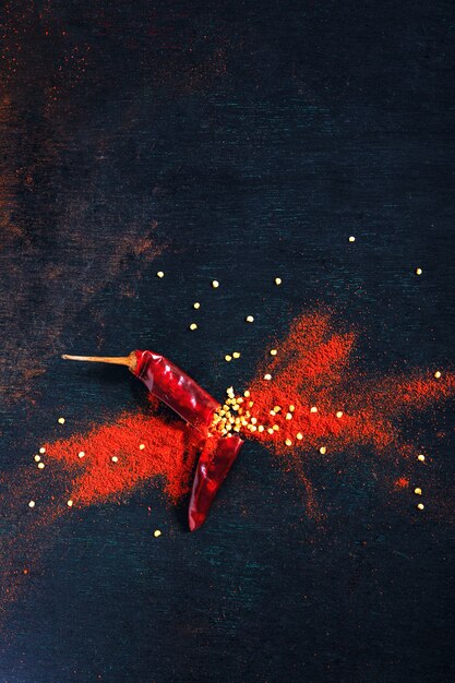 Rode chili peper vlokken en chili poeder barsten op zwarte achtergrond