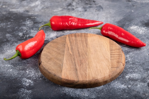 Rode chilipepers met houten snijplank op marmer.