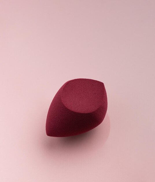 Rode cosmetische spons in de vorm van een ei op een roze achtergrond