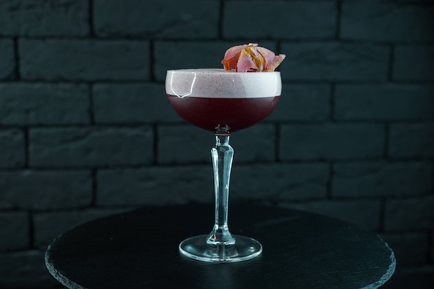 Rode cranberry dubbellaagse heerlijke zoete cocktail met tonic en wodka met bessenlikeur met schuim staat op een tafel tegen een zwarte achtergrond. Originele alcoholische cocktails. Weekend aan de bar