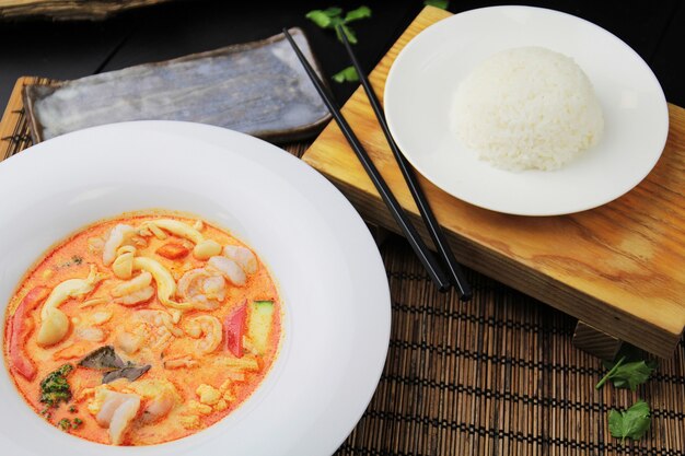 Rode curry met garnalen op een witte plaat, rijst en eetstokjes