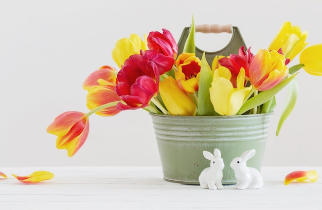 Rode en gele tulpen in emmer en ceramisch konijn op witte achtergrond