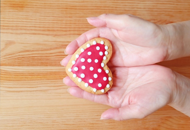 Rode en witte hartvormige royal icing cookie in de hand van de vrouw op houten achtergrond