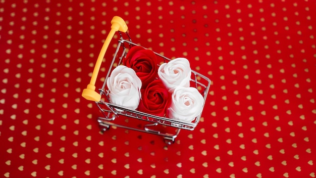 Rode en witte rozen bloem op winkelwagentje op rode achtergrond. Winkelvakantie voor Valentijnsdag liefdesconcept