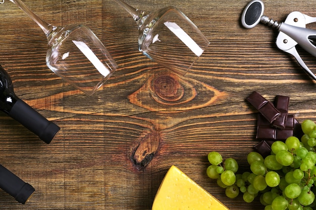 Rode en witte wijnflessen, druiven, kaas en glazen over houten tafel. bovenaanzicht met kopie ruimte. stilleven. plat leggen