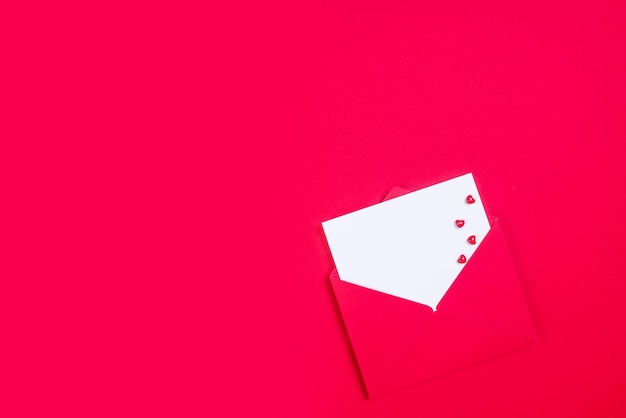 Rode envelop met witte papieren ansichtkaart mockup en kleine harten voor de vakantie