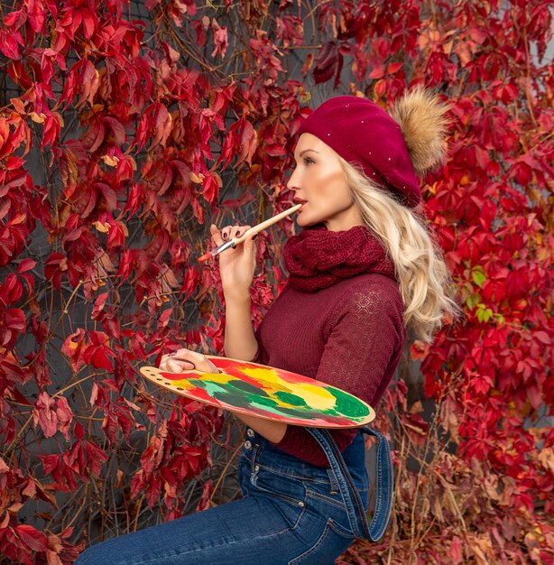 Foto rode esdoornbladeren vrouwelijke kunstenaar tekent op de bladeren in een spijkerbroek en een bordeauxrode trui