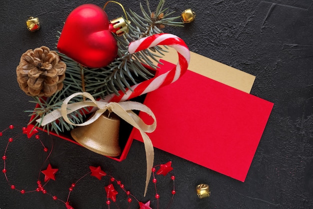 Rode geschenkdoos met een kerst speelgoed in de vorm van een hart, dennentakken, kerst snoep, slinger en kaart voor felicitatie tekst op de zwarte achtergrond