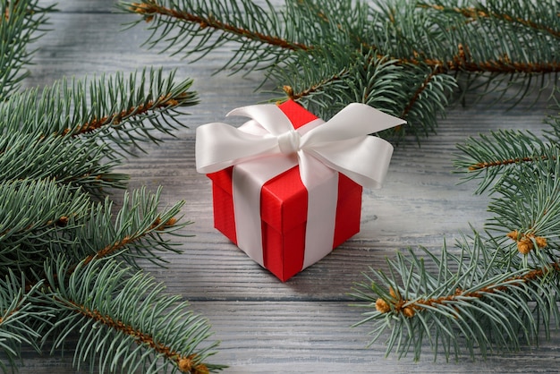 Rode geschenkdoos met een strik op een houten oppervlak tussen de fir takken. Concept voor kerstverrassingen en geschenken.
