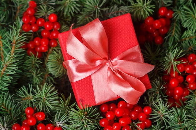Rode geschenkdoos met satijnen roze strik, ondergedompeld in de naalden van een kerstboom versierd met rode bessen.