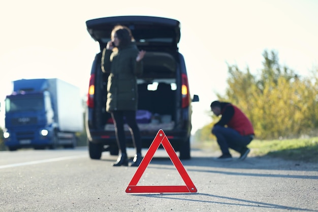 Rode gevarendriehoek op asfaltweg Echtpaar in de buurt van kapotte auto die om hulp roept