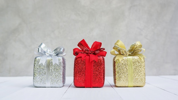 Rode, gouden en zilveren geschenkdoos op een witte houten tafel.