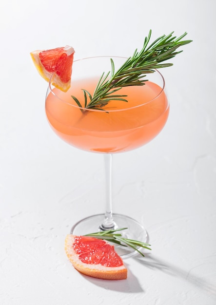 Rode grapefruit zomersap cocktail in modern luxe martini glas met rozemarijn en fruit segment op witte achtergrond