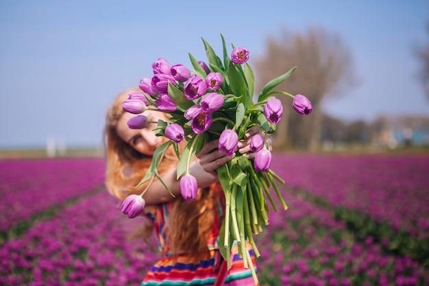 Rode haarvrouw die een kleding draagt die een mand met boeket van tulpenbloemen houdt