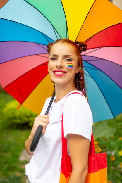 Rode haarvrouw met lgbt vlag bij haar gezicht het stellen met regenboogparaplu