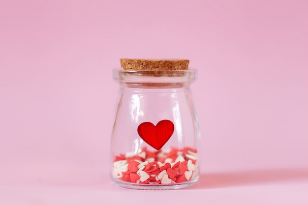 Rode harten in een glazen pot op roze muur.