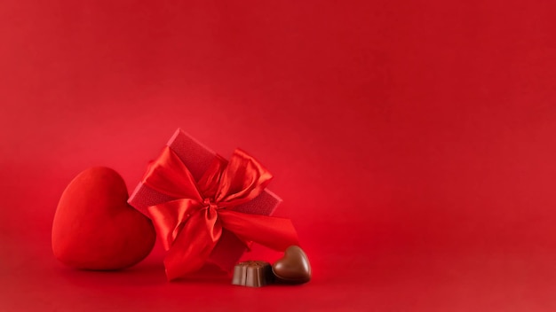 Rode hartfiguur huidige doos en chocoladetruffels tegen rode achtergrond Sint-Valentijnsdag