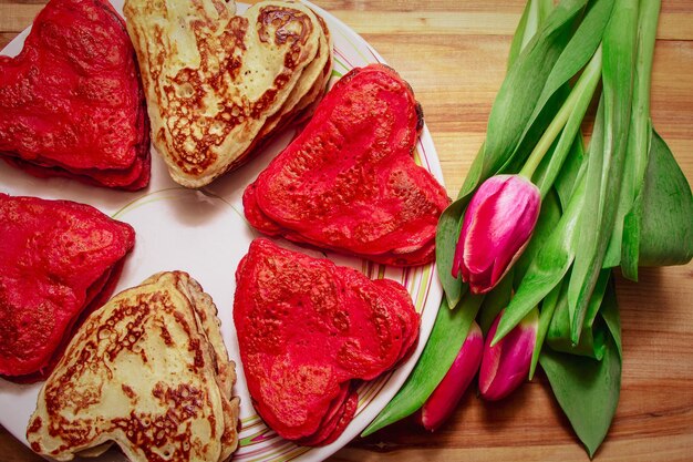 Rode hartvormige pannenkoeken gemaakt met liefde voor Valentijnsdag en tulpen op houten achtergrond