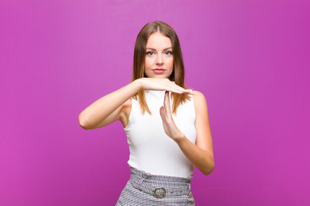 Rode hoofd mooie vrouw die ernstig, streng, boos en ontstemd kijken, die tijd maken uit ondertekenen tegen purpere muur