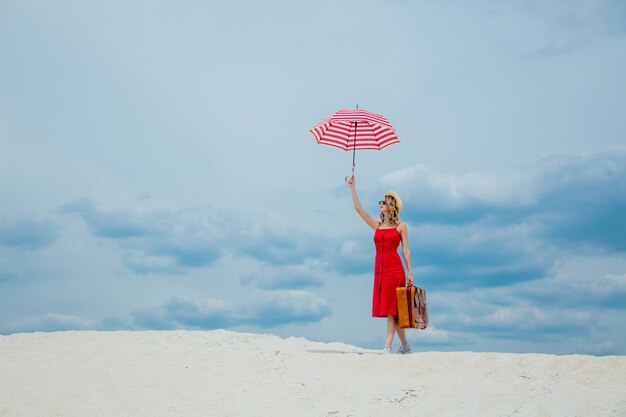 Rode jurk met paraplu en koffer op het strand