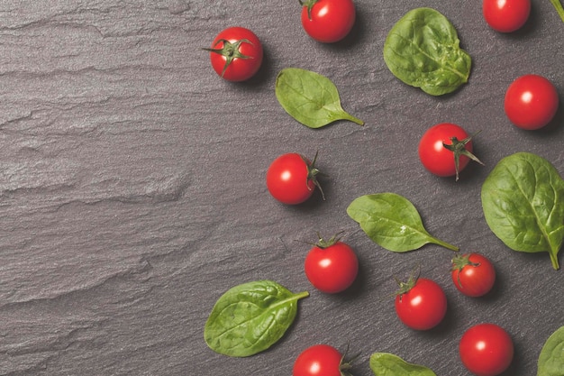 Rode kersentrostomaten en groene saladebladeren op een leiachtergrond