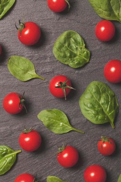 Rode kersentrostomaten en groene saladebladeren op een leiachtergrond