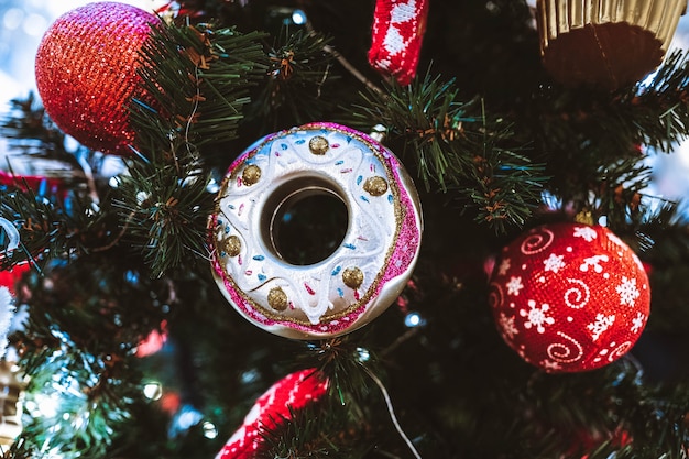 Rode kerstballen en donut hangen aan de kerstboom. Feestelijke inrichting in interieur. Nieuwjaarsdetails en sfeer