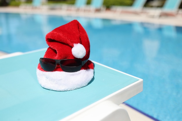 Rode kerstman hoed en zonnebril liggend op de ligstoel aan de oever van het zwembad close-up