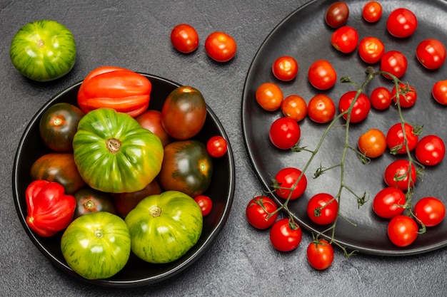 Foto rode kerstomaten op een takje groene tomaten in zwarte platen