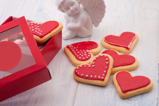 Rode koekjes in de vorm van een hart in een geschenkdoos en engelen op houten planken