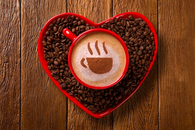 Rode kop en koffieschotel in hartvorm met gedecoreerde koffie op oude houten ruimte. Bovenaanzicht. bekervorm in koffie.