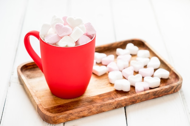 Rode kop warme chocolademelk met hartvormige marshmallows op witte houten achtergrond