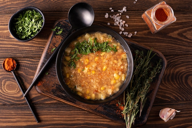 Rode linzen en maïs soep met kruiden en paprika in een zwarte kom op een houten tafel