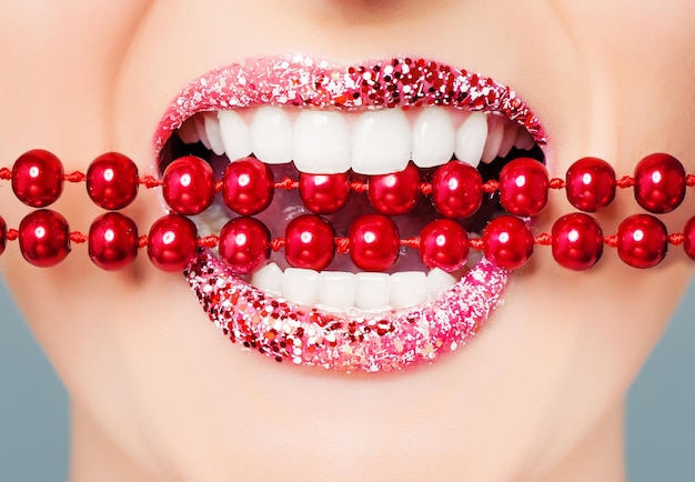 Rode lippen en witte gezonde tanden met heldere parels close-up Perfecte vrouwelijke glimlach met glitter lippenstift make-up