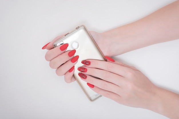 Rode manicure met een patroon. Slimme telefoon in vrouwelijke hand. Wit