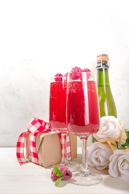 Rode mimosacocktail voor valentijnsdag. klassieke mimosa drank met frambozensap, framboos en munt decor. met geschenkdoos voor valentijnsdag, rozenbloemen, champagnefles