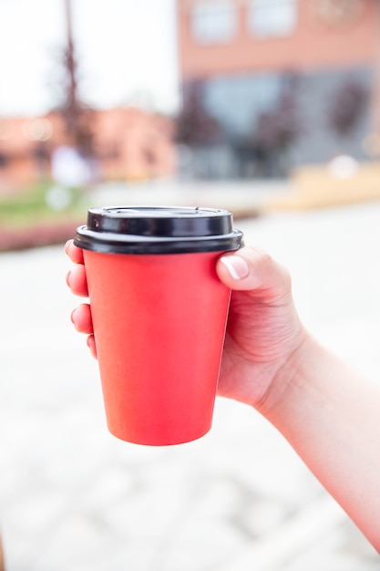 Rode papieren kopje koffie om mee te nemen in de hand van de vrouw. Zonnig weer. Ontbijt ochtend in de lucht