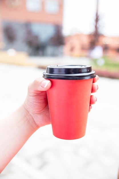 Rode papieren kopje koffie om mee te nemen is in de hand van de vrouw