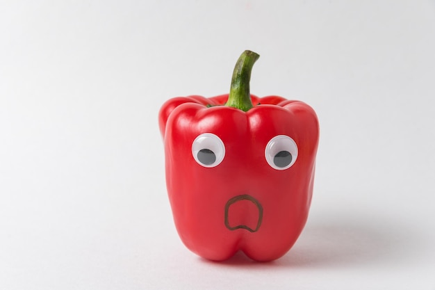 Foto rode paprika met grappig gezicht peppersmiley met googly-ogen op witte achtergrond