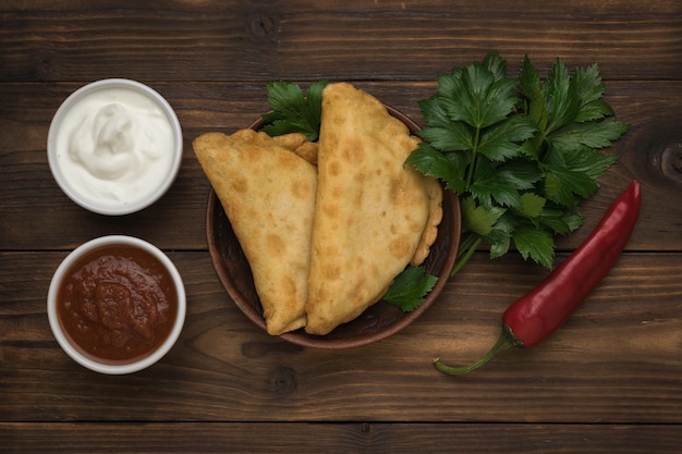 Rode peper twee chebureks en twee soorten saus op een houten tafel