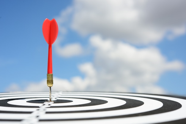 Rode pijltjepijl die in het doelcentrum van dartboard met blauwe hemelachtergrond raakt