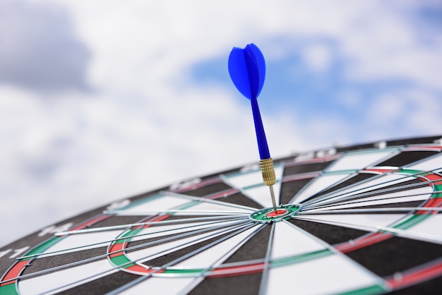 Rode pijltjepijl die in het doelcentrum van dartboard met blauwe hemelachtergrond raakt